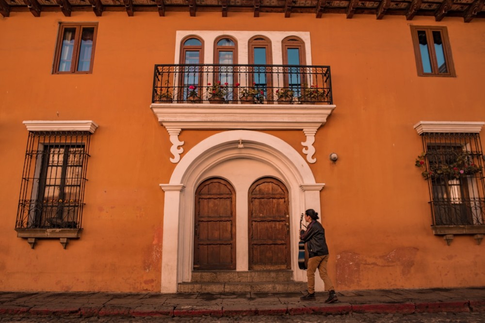 hombre con guitarra camina frente a un portón en Antigua, Guatemala