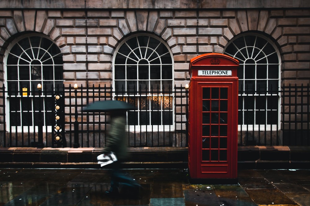 hombre con paraguas pasa frente a cabina telefónica en Londres