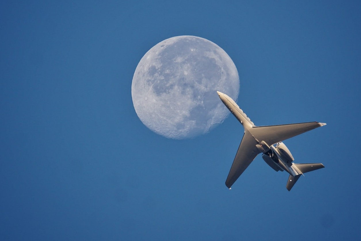 avión visto desde abajo pasando frente a la Luna