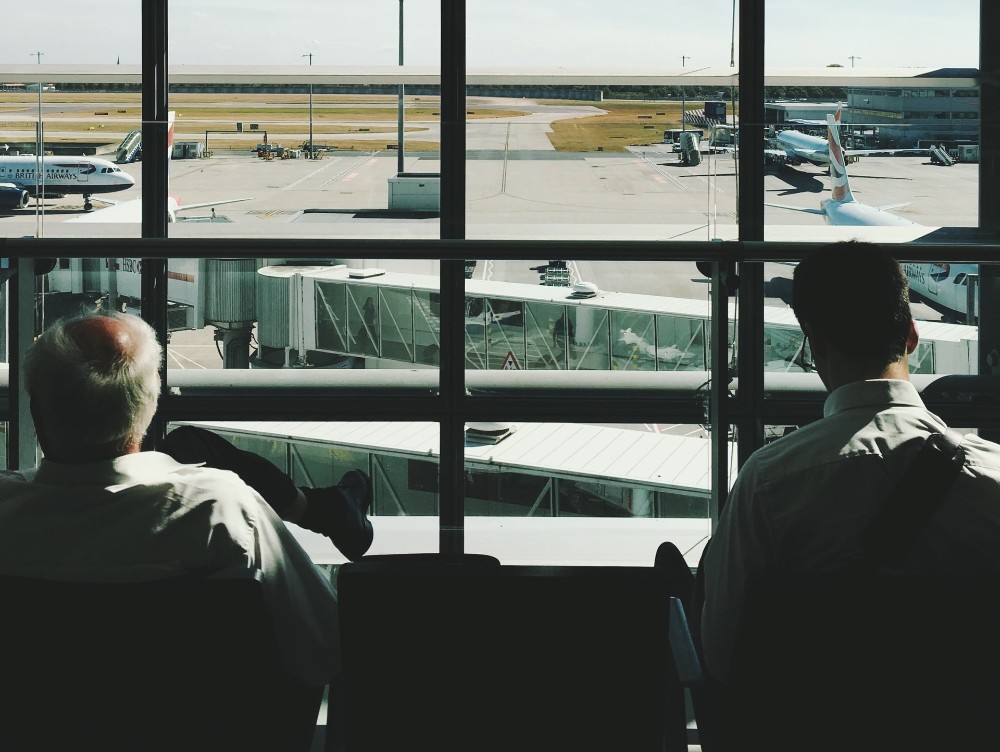 dos pasajeros sentados de espalda en la terminal de Heathrow, mirando la pista