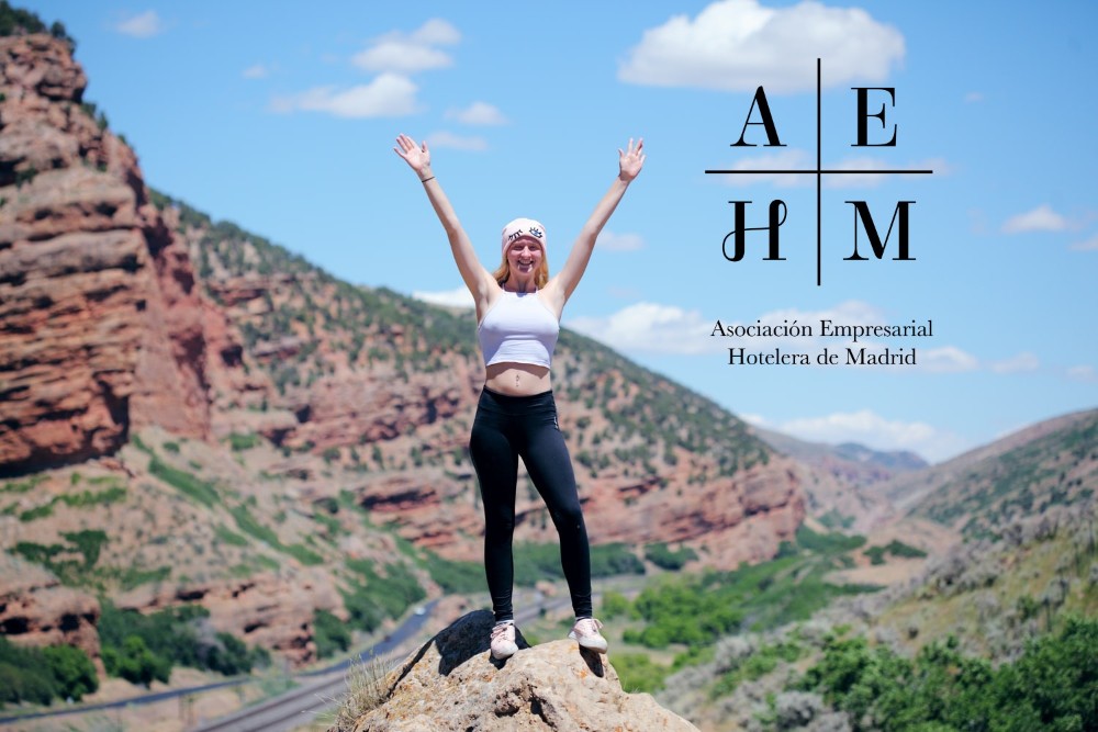 mujer con los brazos en alto en una montaña y logo de la AEHM