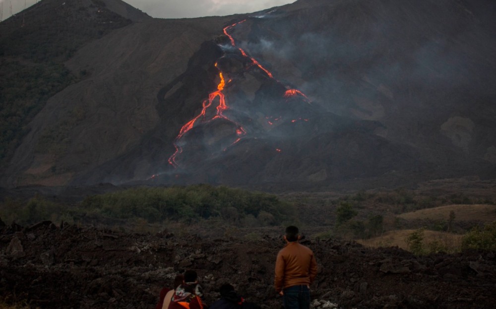 Volcán Pacaya en Guatemala, lava bajando por la ladera, dos hombres observan en primer plano