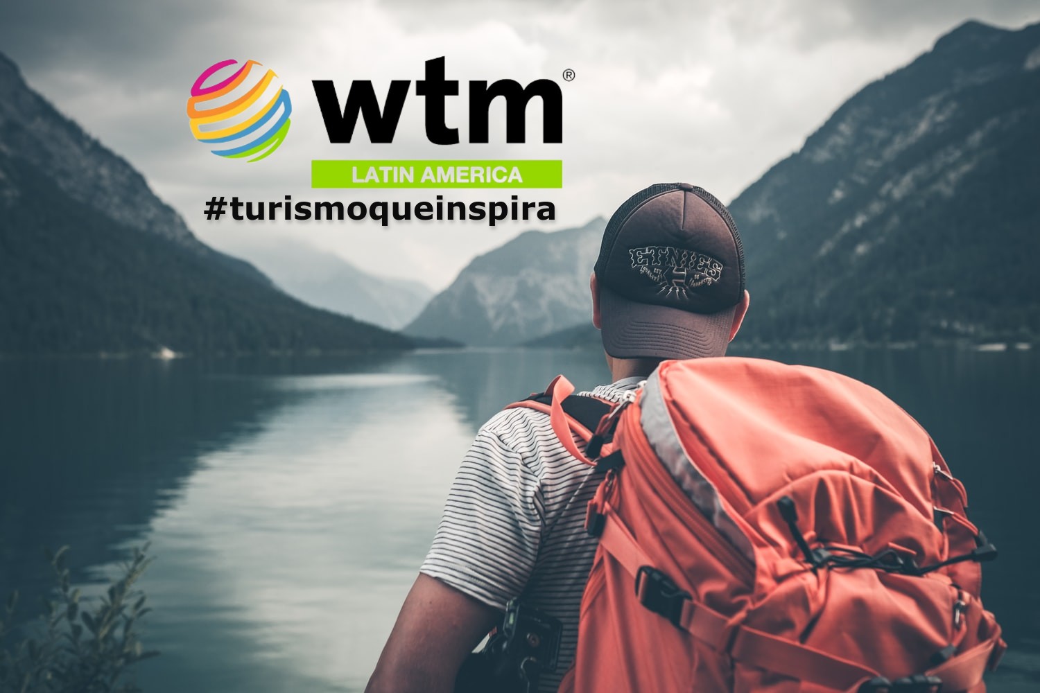 turista con gorra y mochila, de espalda, mirando un lago entre montañas, sello de WTM Latin America y hasgtag de la campaña