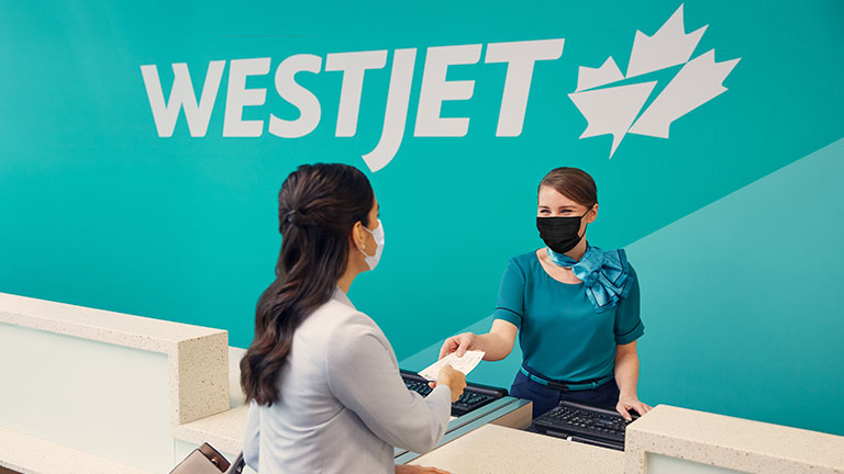 WestJet mostrador, cliente y empleada, logo de WestJet detrás