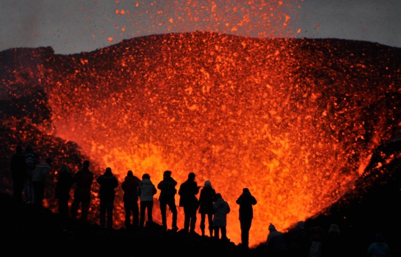 turistas frente a un volcán en erupción, de noche